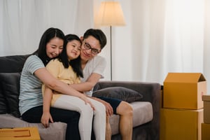 happy-asian-young-family-homeowners-bought-new-house-japanese-mom-dad-daughter-embracing-looking-forward-future-new-home-after-moving-relocation-sitting-sofa-with-boxes-together